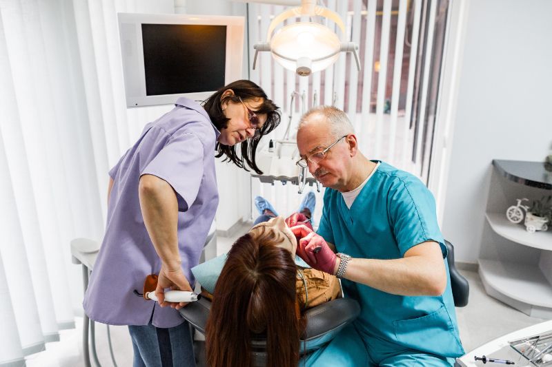 A dentist and a nurse are examining a patient 's teeth in a dental office.