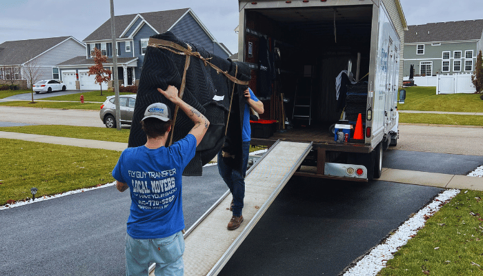 A man in a blue shirt is carrying a large piece of furniture into a truck.