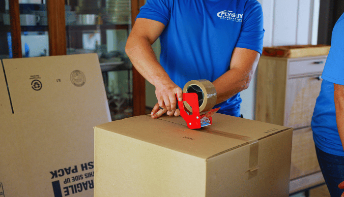 A man is taping a cardboard box with tape.