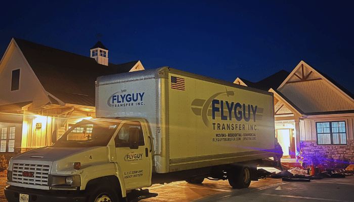 A yellow moving truck is parked in front of a house at night.