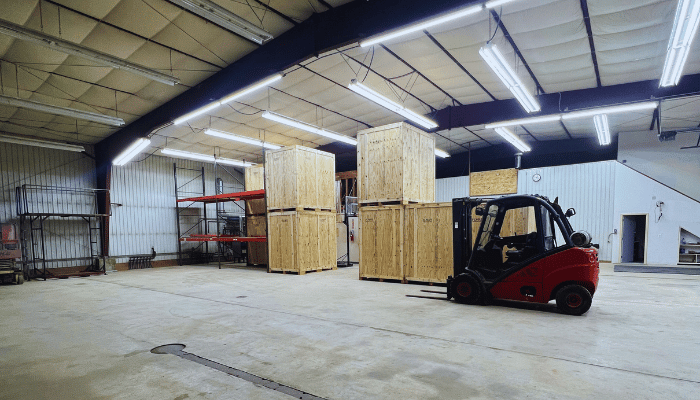 A red forklift is moving wooden crates in a large warehouse.