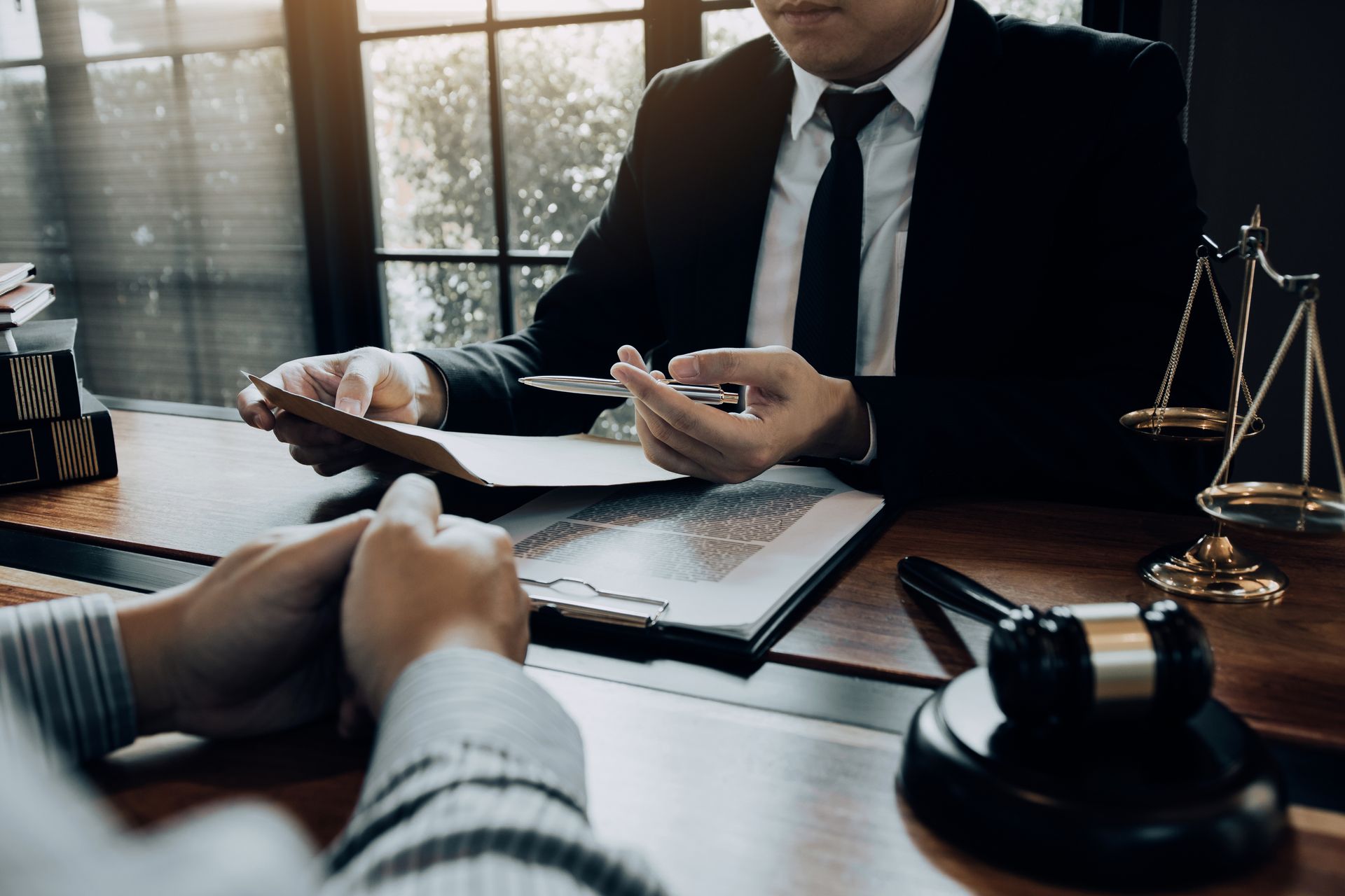 Lawyer in a dark suit reviewing documents across a desk with a client, gavel and scales nearby