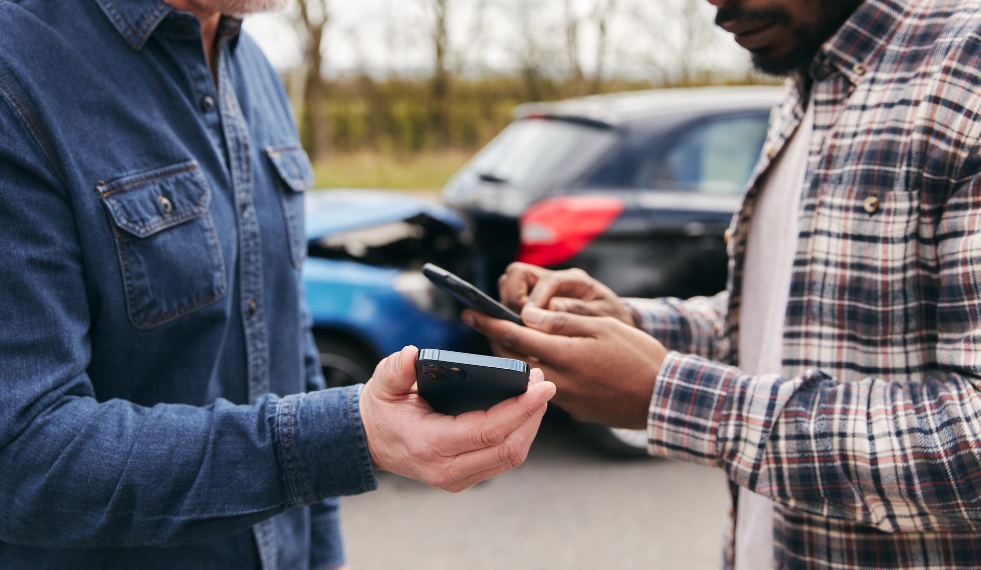 Two people comparing smartphones outdoors beside a parked car