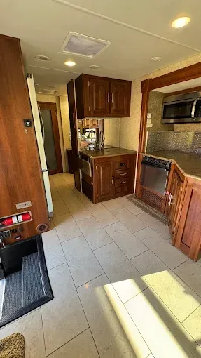 Interior of an RV kitchen with wooden cabinets, a sink, and an oven, with tile flooring.