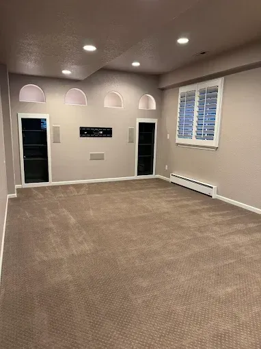 Empty room with tan carpet, built-in shelves, and shuttered window.