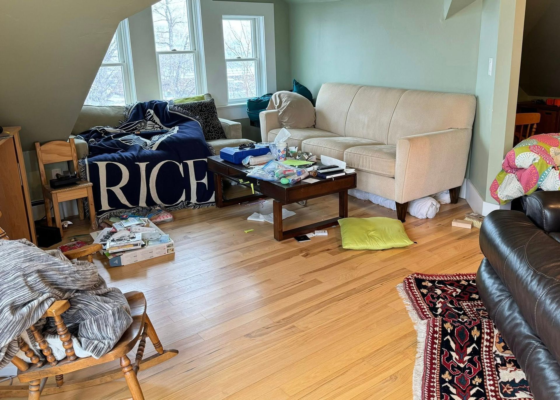 Messy living room with couch, coffee table, and windows; items scattered on floor.