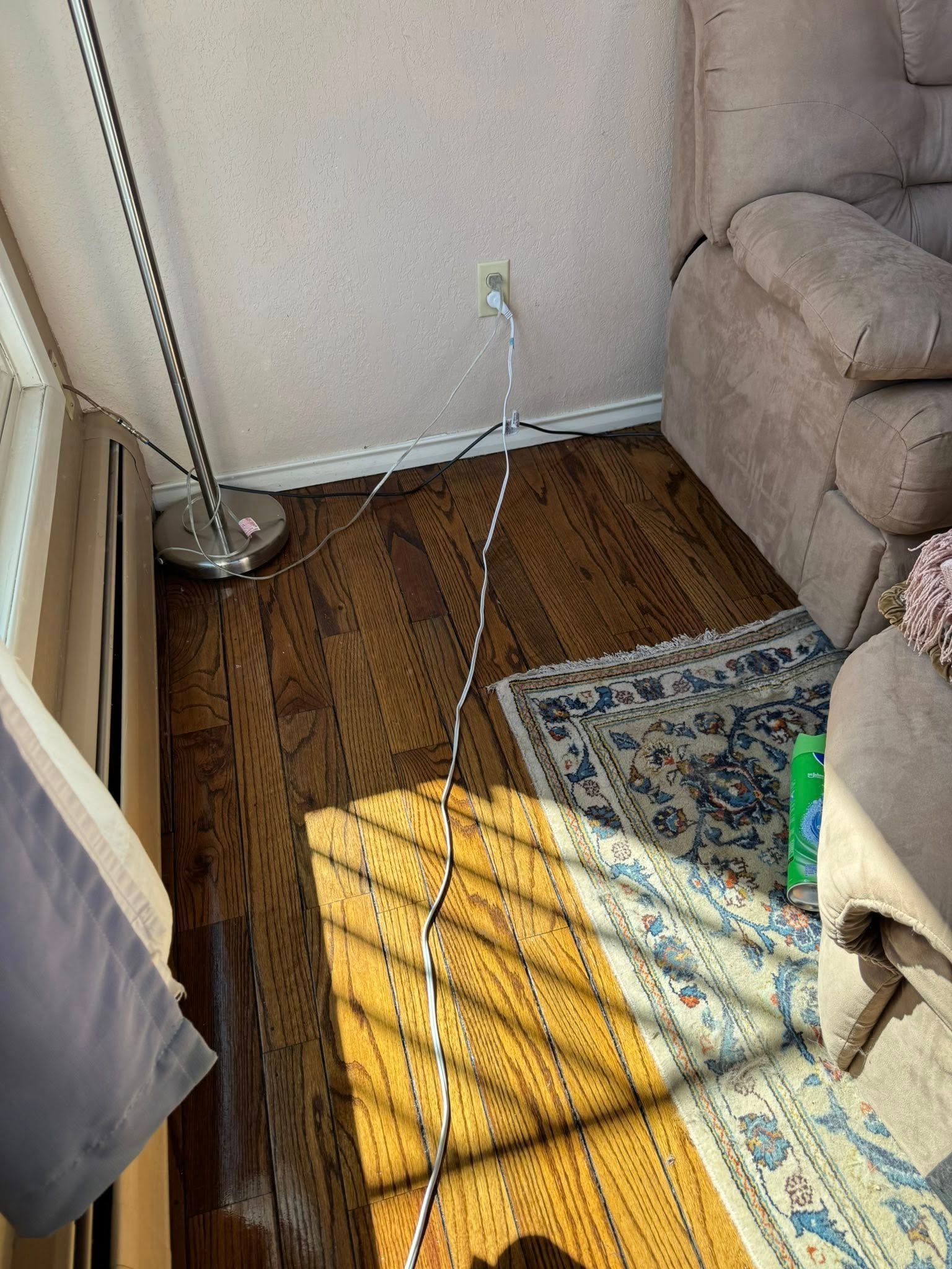 Hardwood floor with rug, lamp, recliner, and power outlet. Light and shadows.
