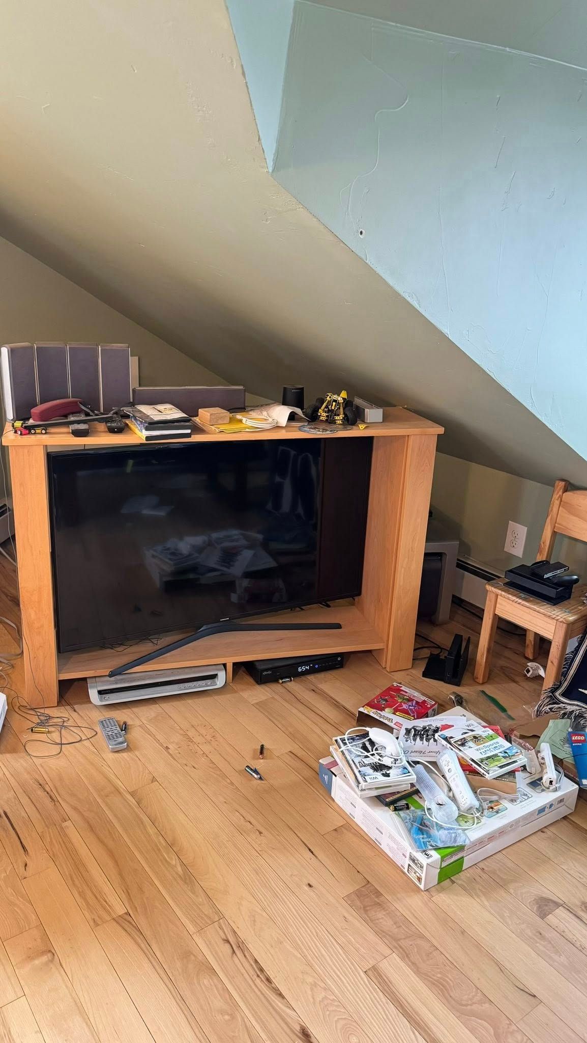 A wooden TV stand with a TV on it, in a room with light wood floors. The room is messy.