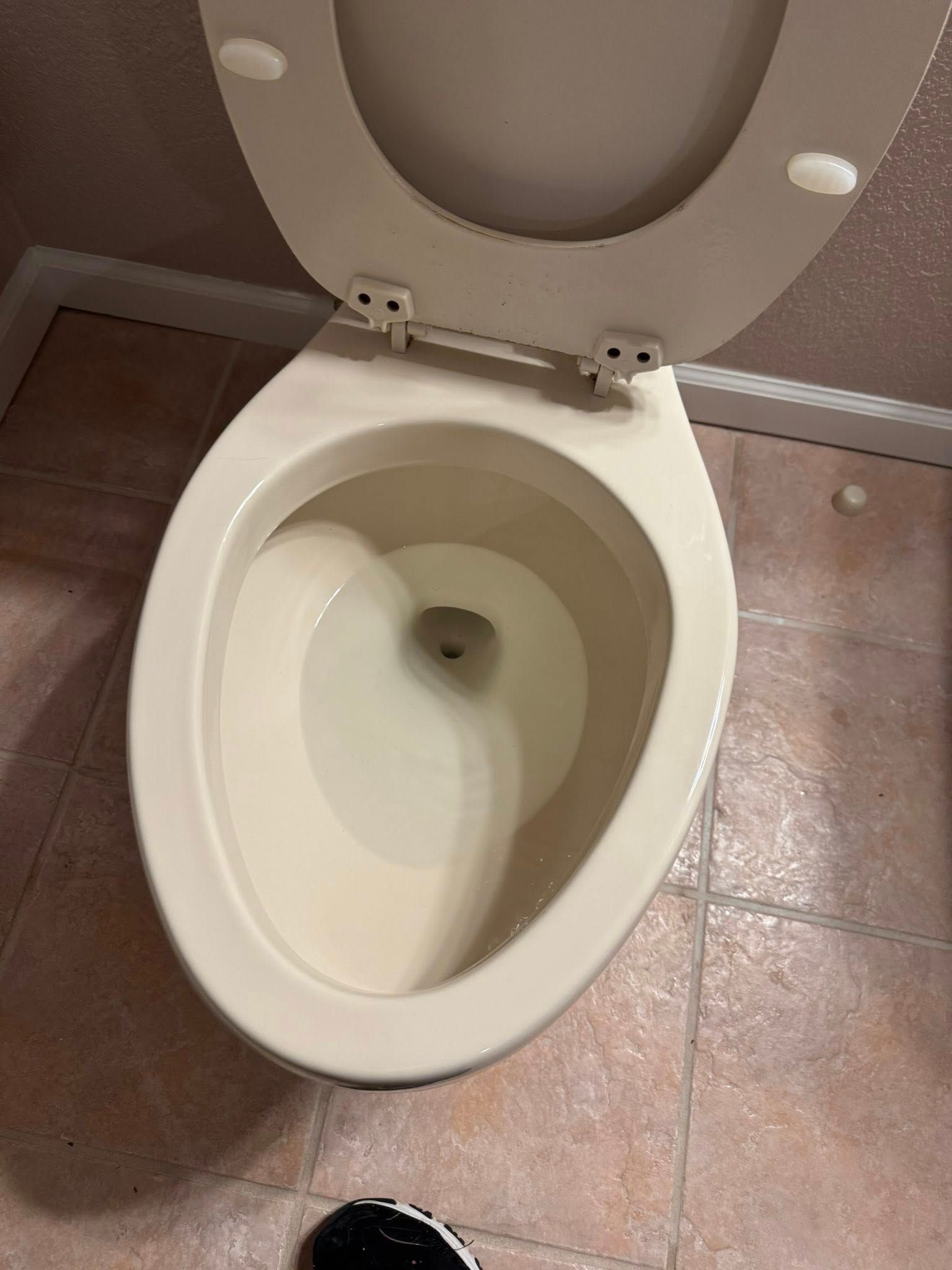 An open, off-white toilet with water, in a tiled bathroom.