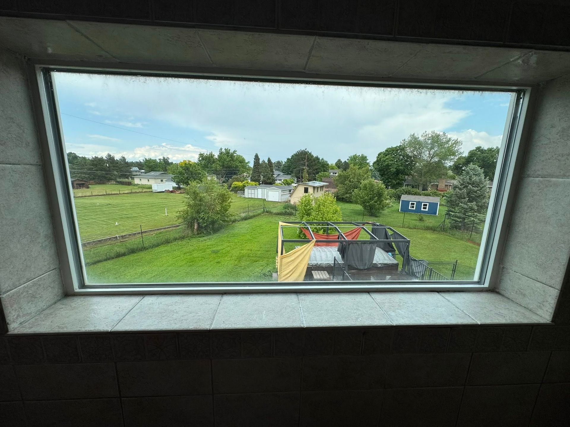 View through a window of a green yard, trees, houses, and a blue sky.