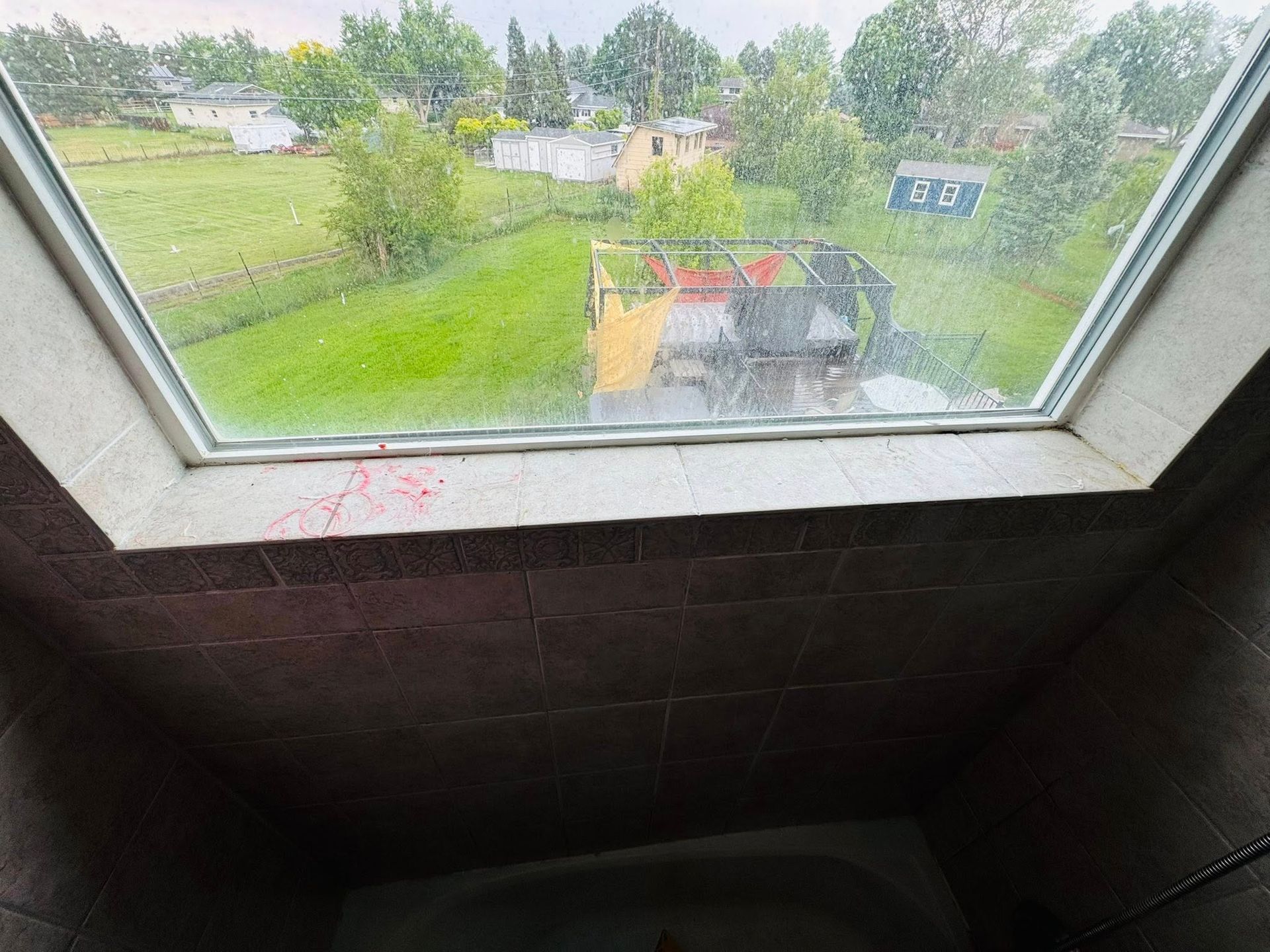 Bathroom with a skylight and a view of a green yard and houses. Tiles and a bathtub are visible.