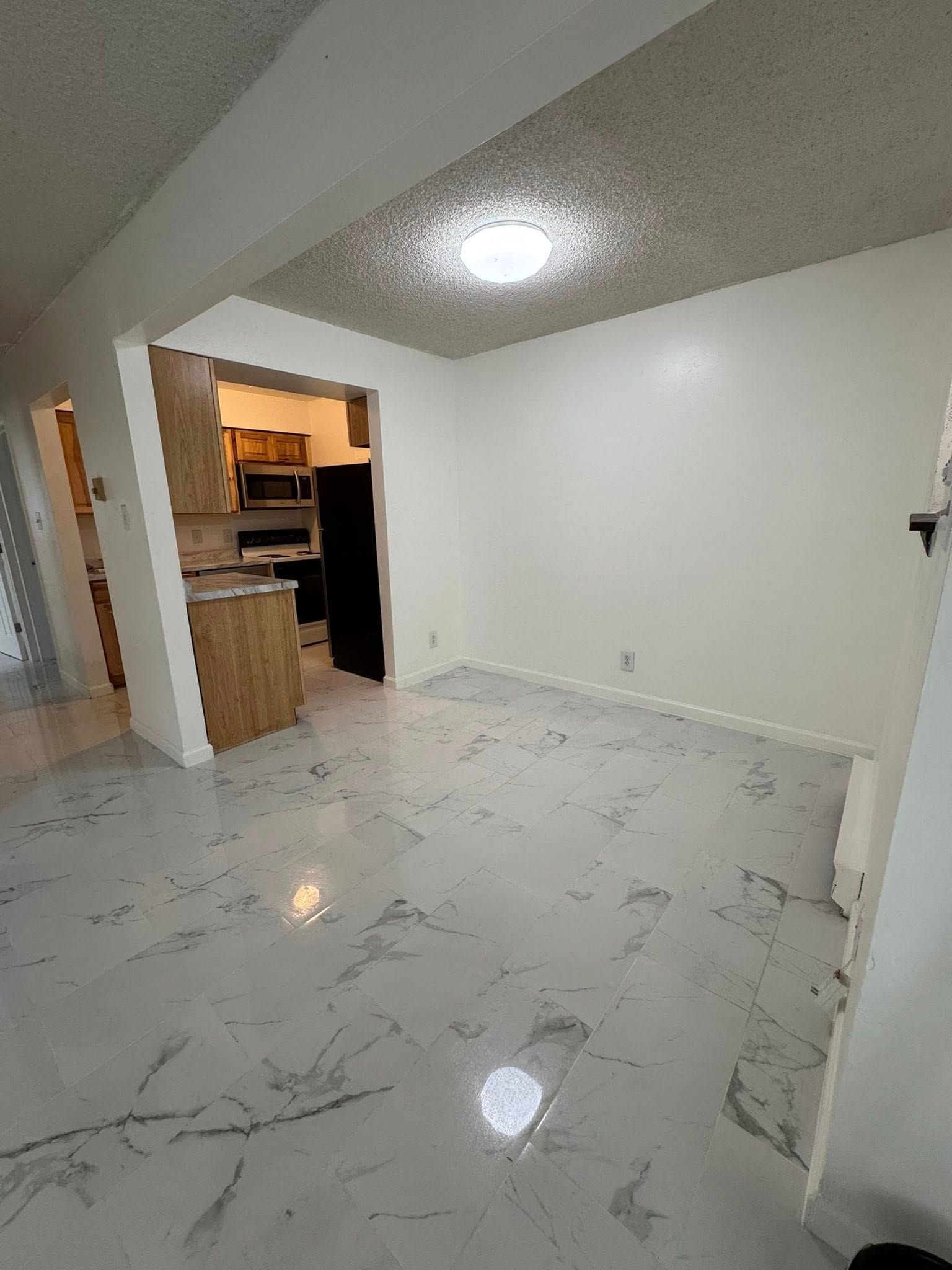 Interior view of a room with marble floors and white walls; kitchen in the background.