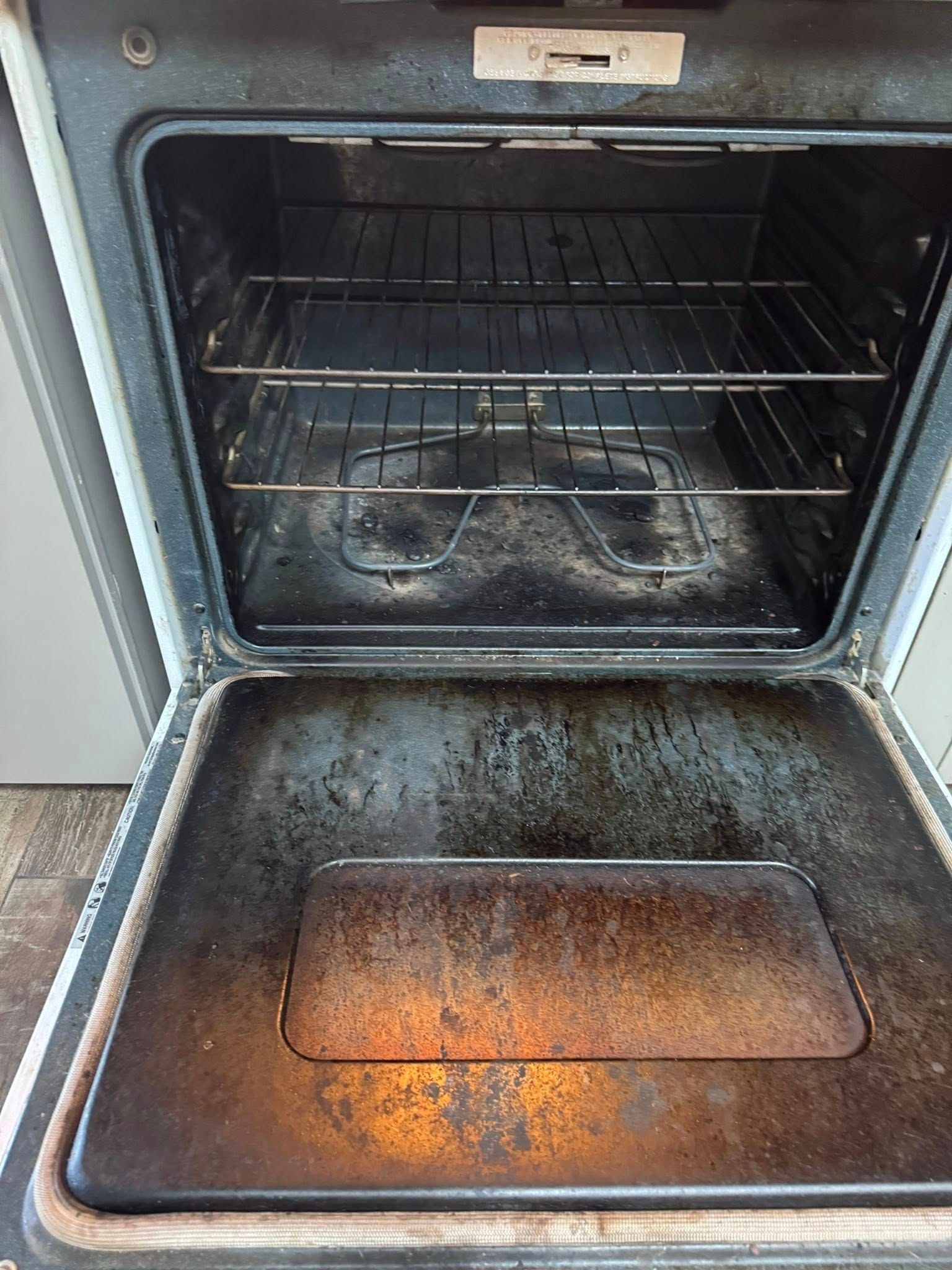 Open, dirty oven interior with racks and spill-covered bottom.