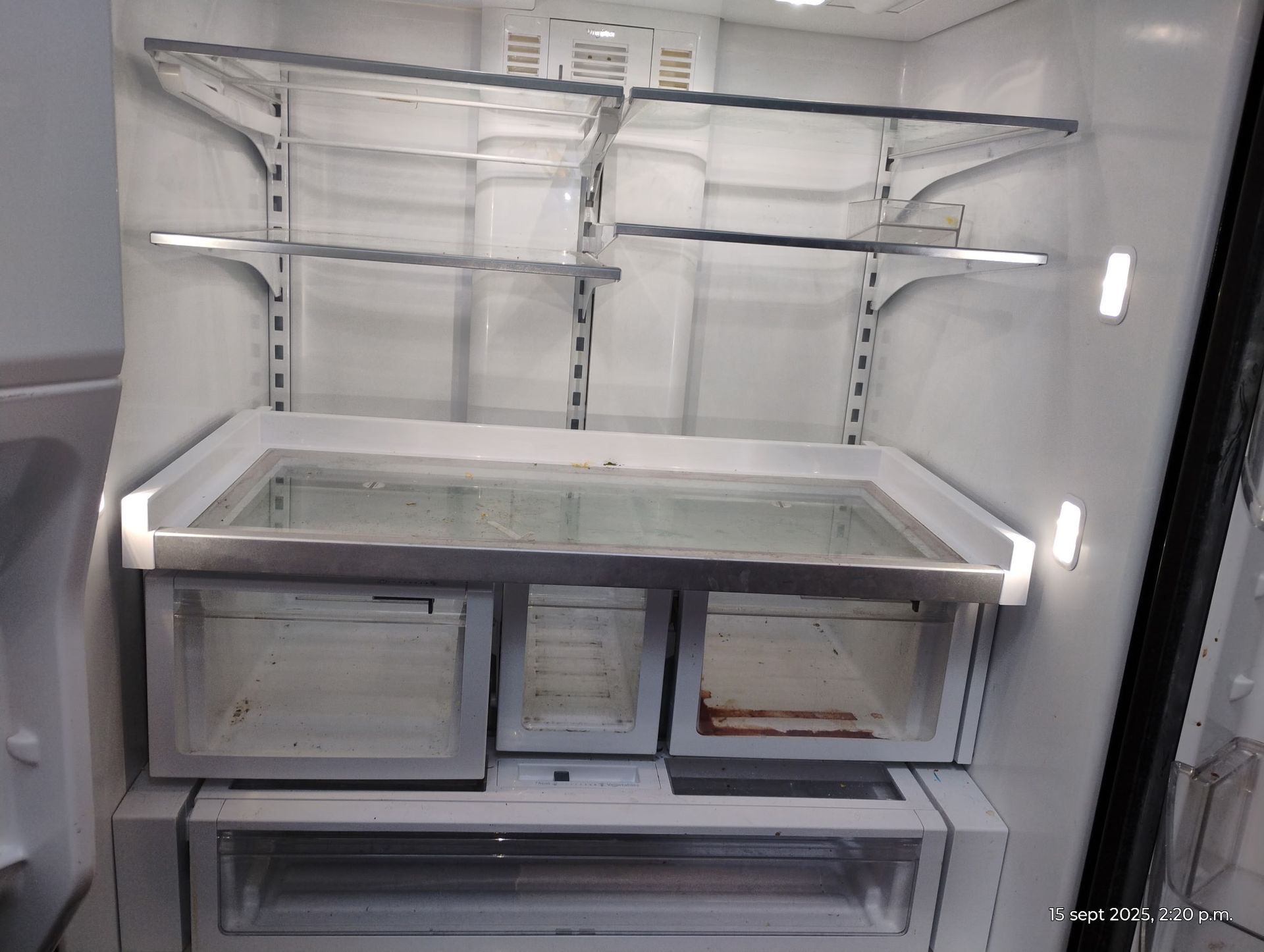 Interior of an empty refrigerator with multiple shelves and drawers, white and stainless steel.