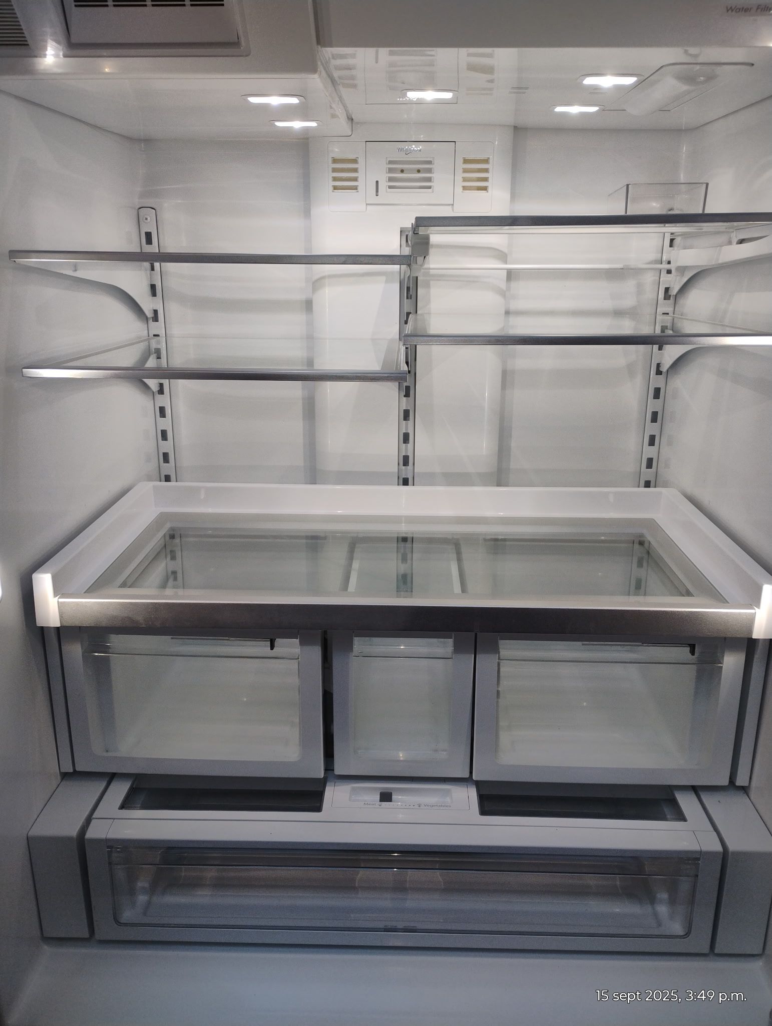 Empty stainless steel refrigerator interior with shelves, drawers, and lighting.