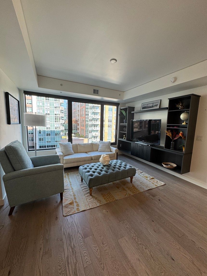 Living room with light-colored sofa, armchair, and ottoman. Dark wood entertainment center and flooring.