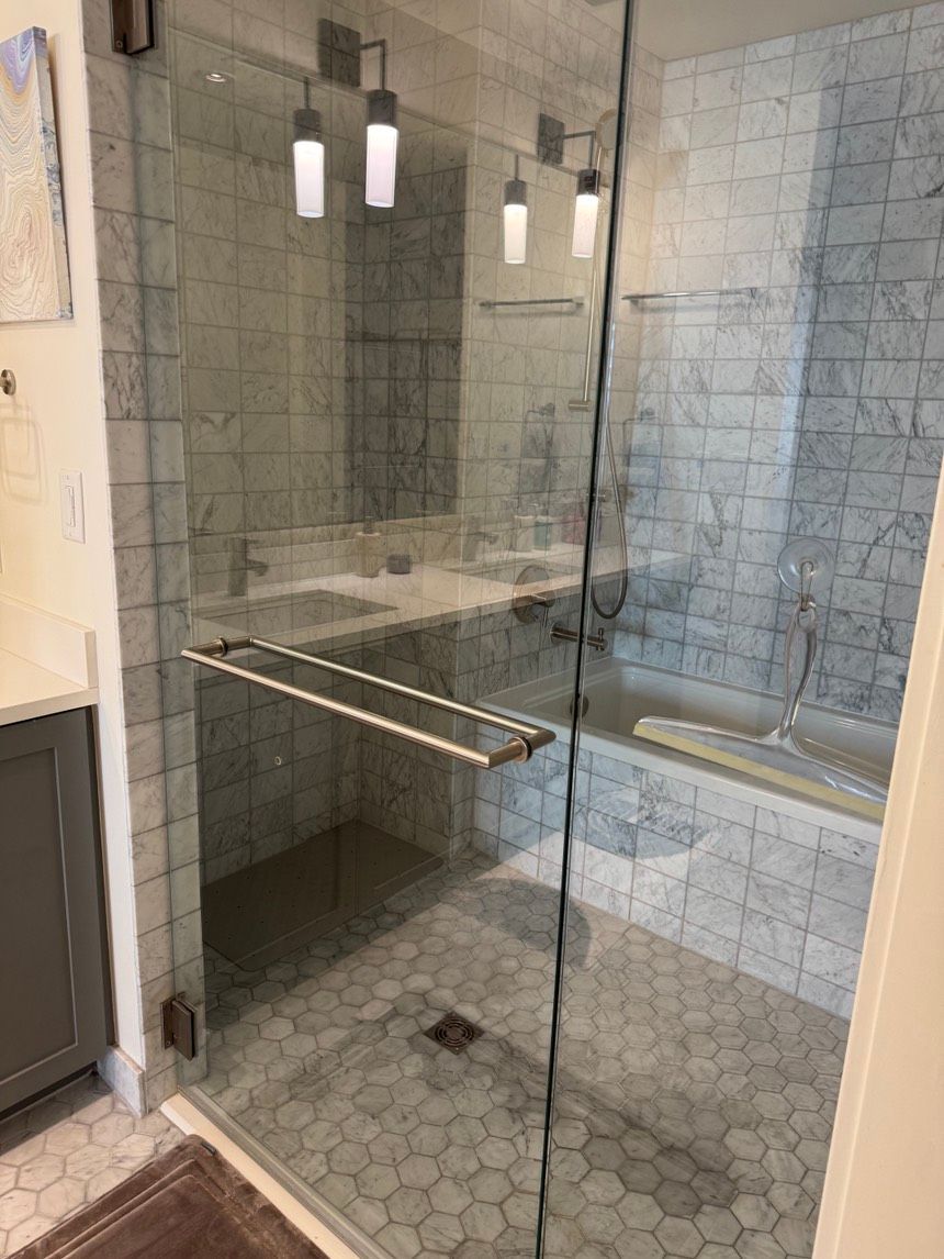 Glass shower with marble tile walls and hexagonal floor tiles.