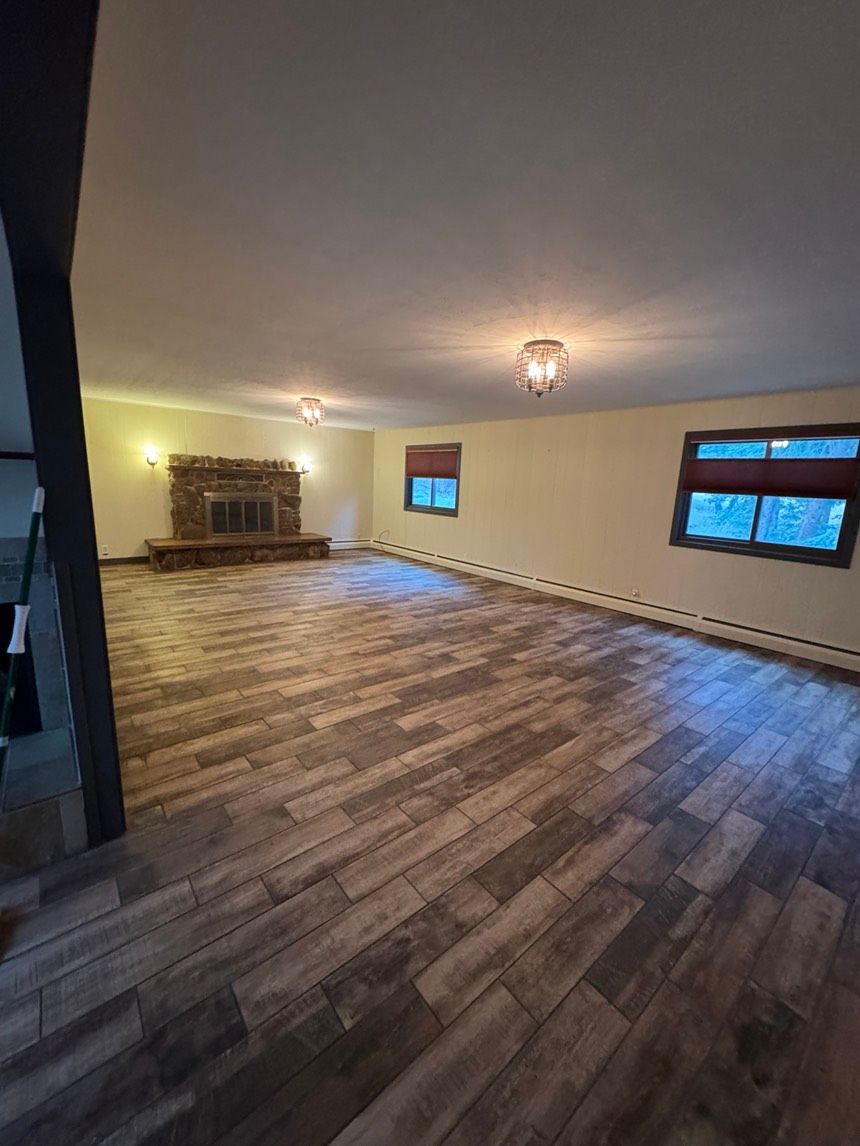 Empty room with wood-look flooring, a fireplace, and two windows. White walls and ceiling.