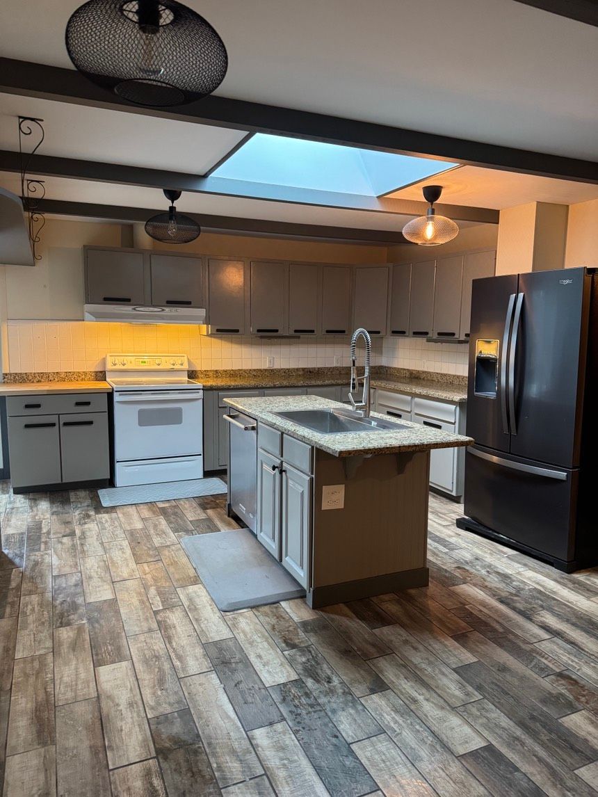 Modern kitchen with gray cabinets, island, and stainless steel appliances. Wooden floor.