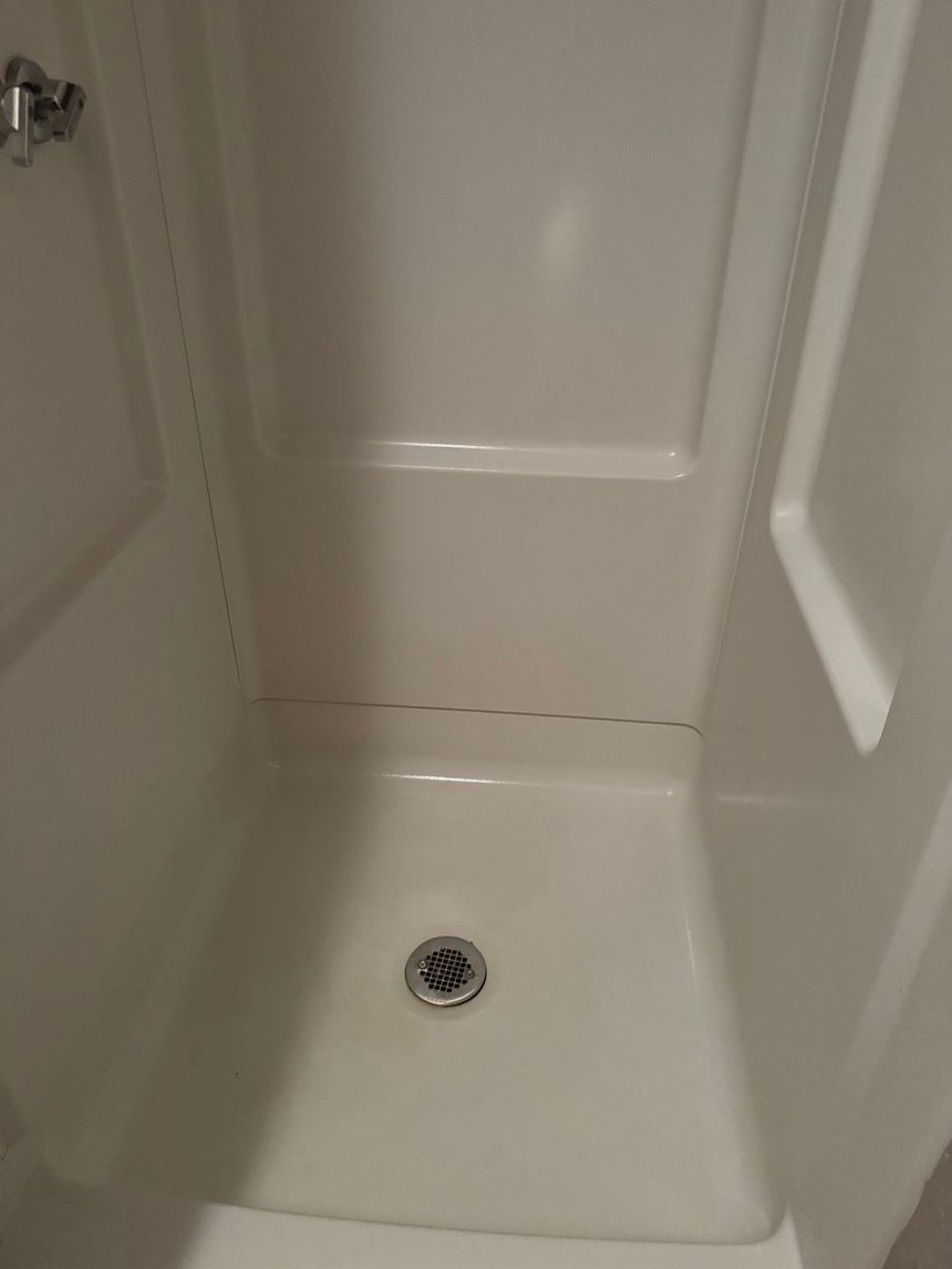 White shower stall with a drain in the floor and a faucet on the left.