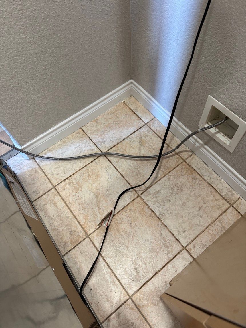 Cables on tiled floor, near a wall and appliance. One wire appears damaged, next to an electrical outlet.