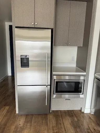 Kitchen with stainless steel refrigerator, built-in microwave, and light gray cabinets against wood flooring.