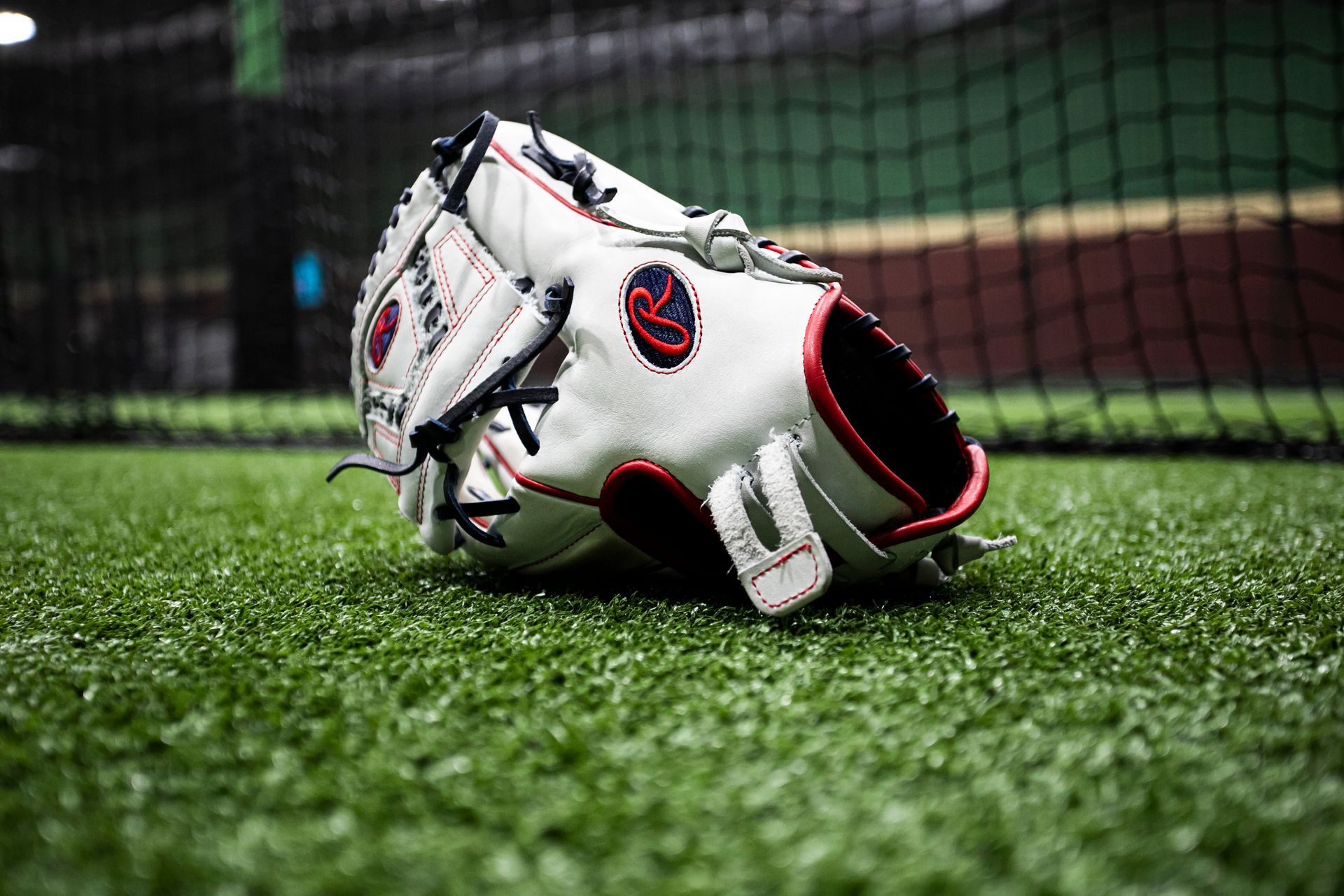 A baseball glove is laying on the grass in front of a net.