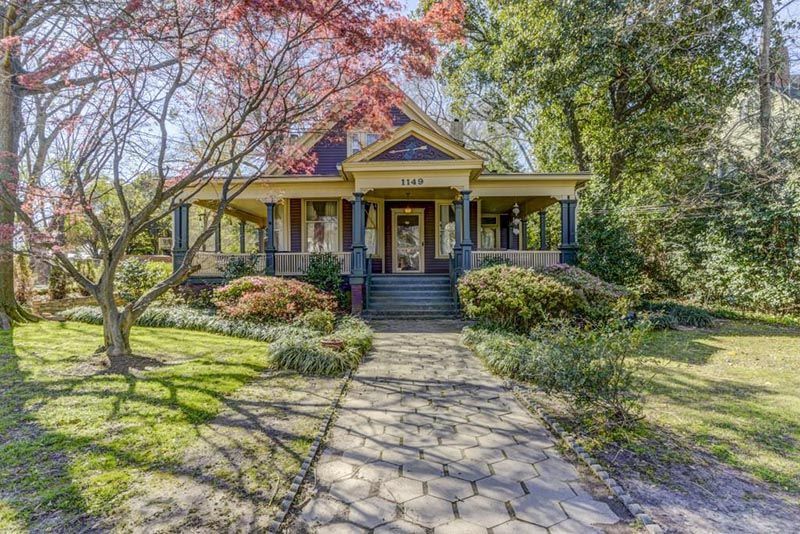 Victorian house with porch and front yard. Beige siding, blue trim. Red tree in the foreground.