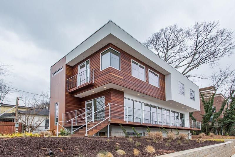 Modern two-story house with wood siding and white accents on a sloped lot under an overcast sky.