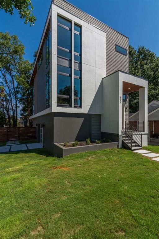 Modern two-story house with gray, white, and dark gray exterior. Large windows, green grass, and blue sky.