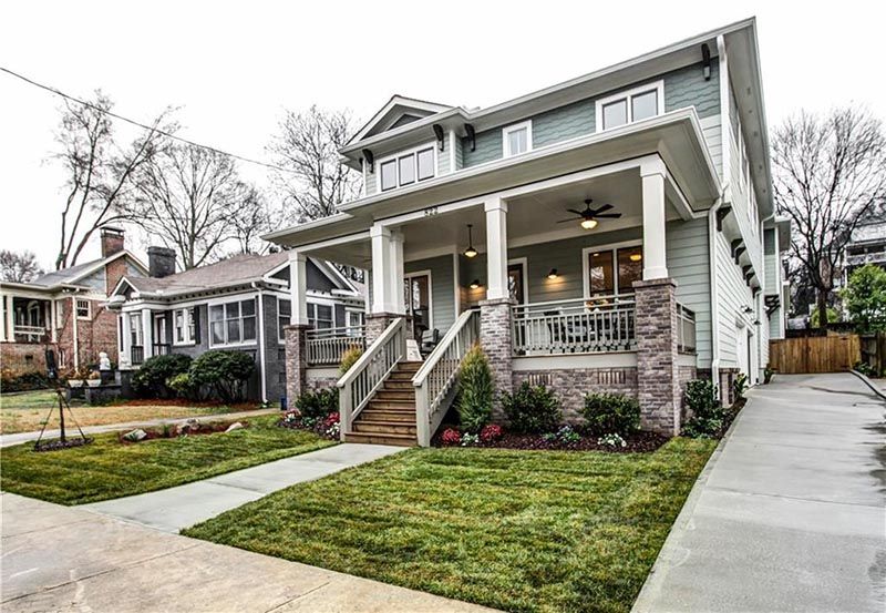 Two-story house with green siding, a covered porch, and a walkway, with grass and other houses nearby.