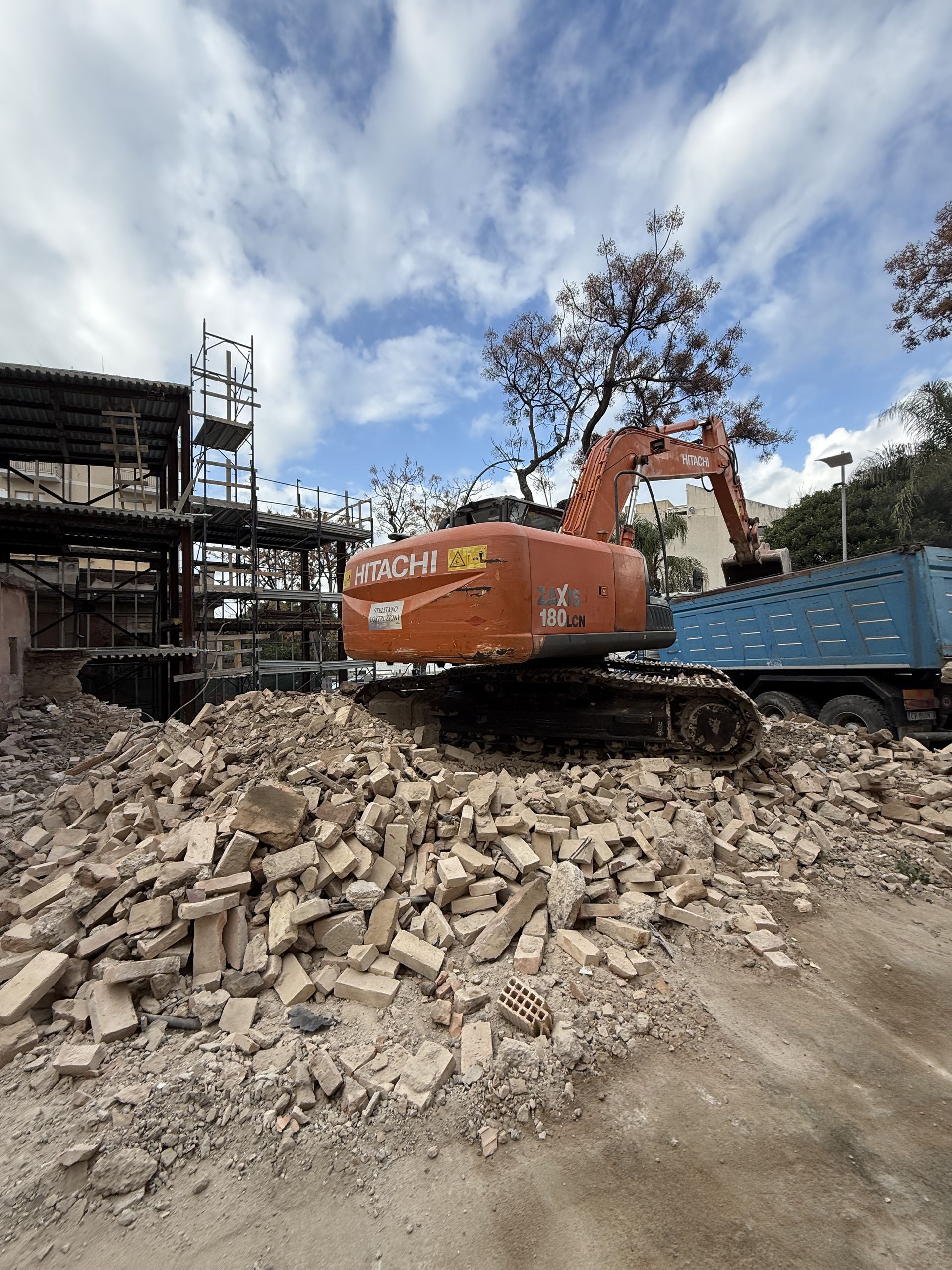 Un grande escavatore arancione è appoggiato su una pila di mattoni.