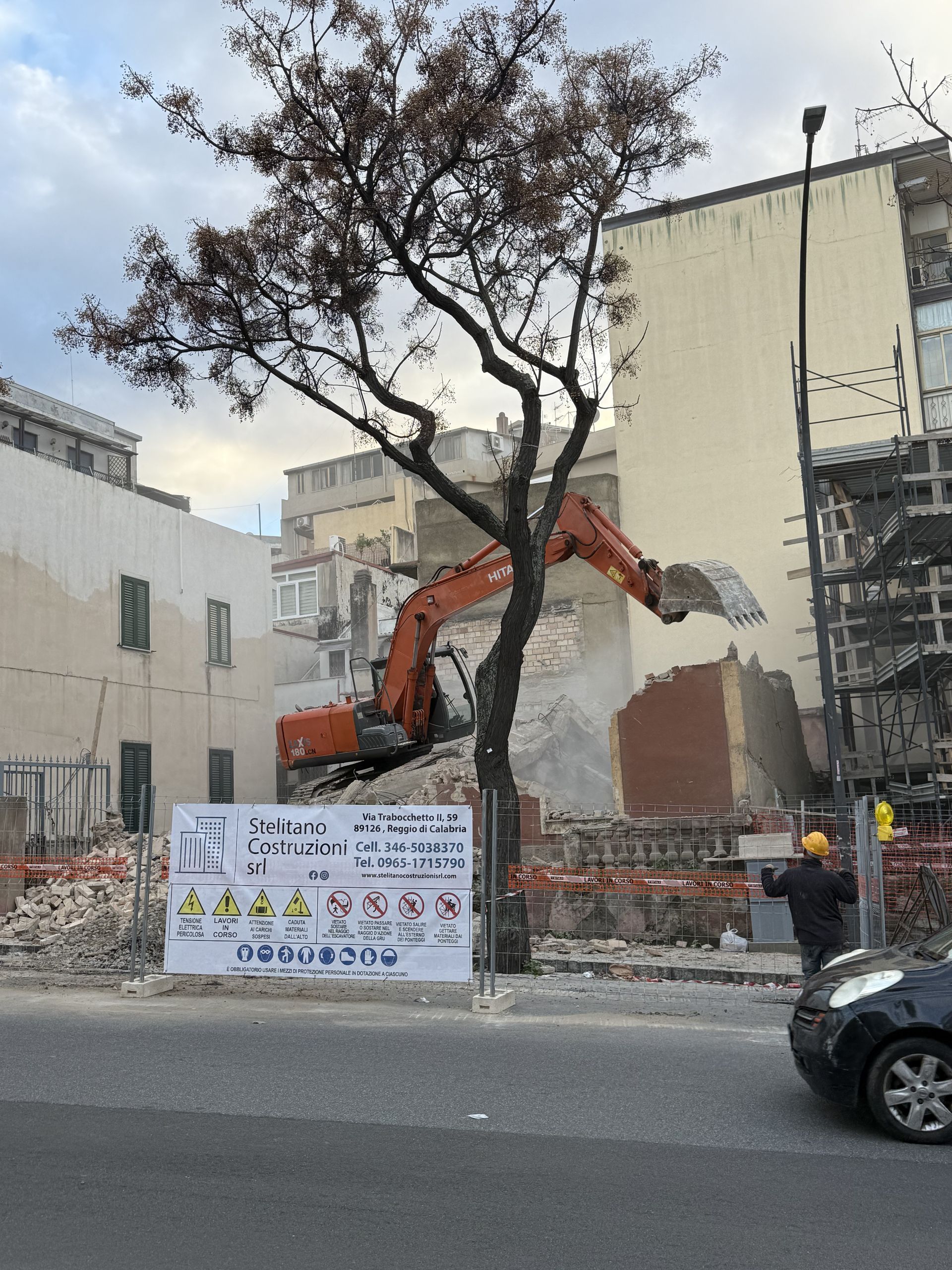 Un escavatore sta demolendo un edificio accanto a un albero
