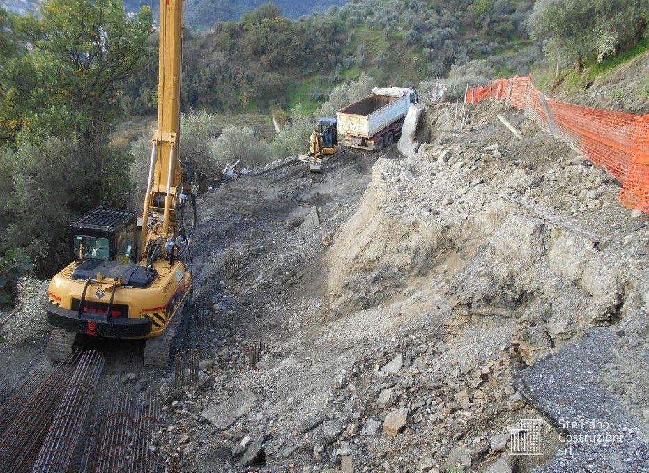 Un escavatore giallo sta percorrendo una strada sterrata accanto a un autocarro con cassone ribaltabile.