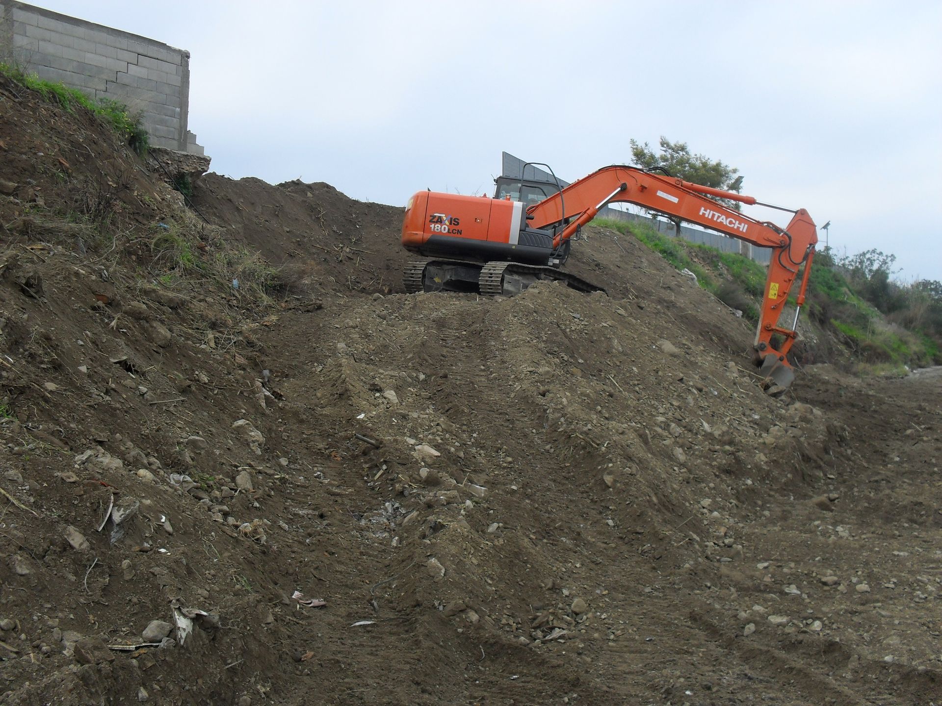 Un grande escavatore arancione è appoggiato su un mucchio di terra.