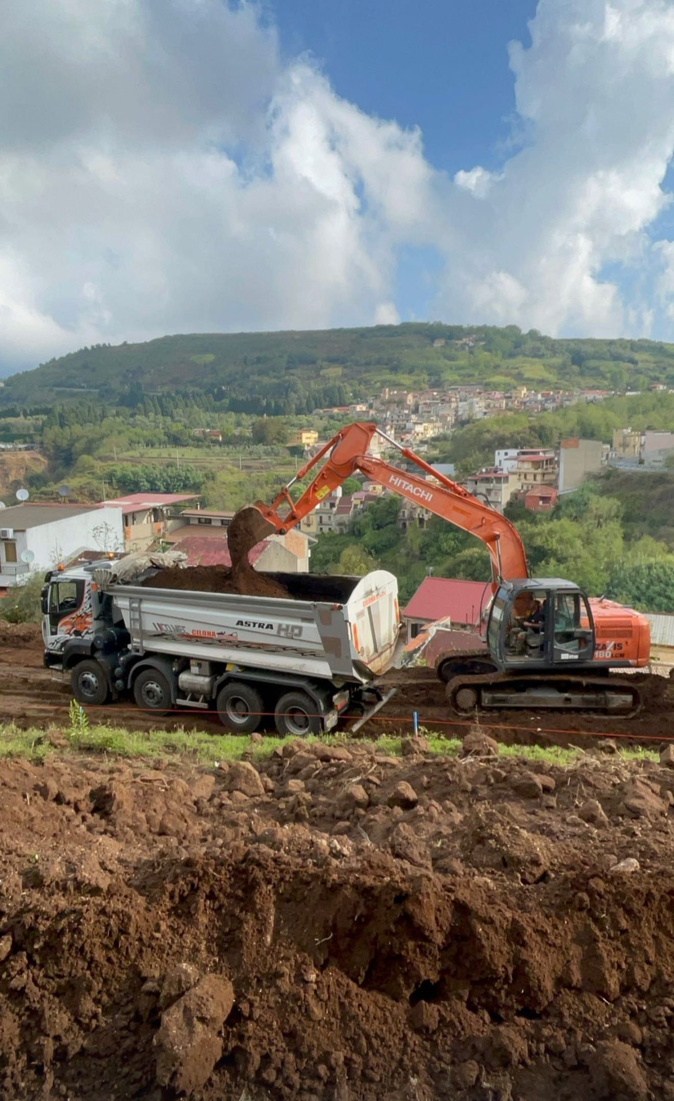 Un camion con cassone ribaltabile viene caricato di terra da un escavatore.