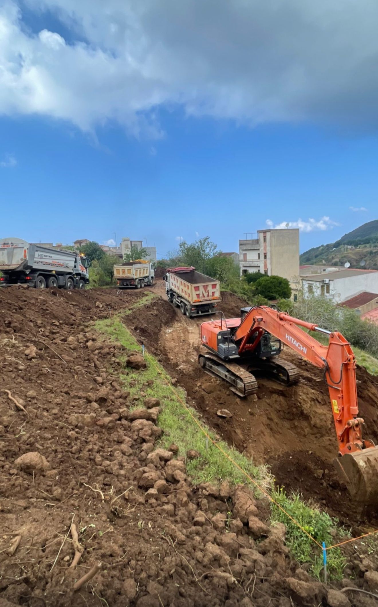 Un grande escavatore arancione sta scavando una buca in un campo sterrato.
