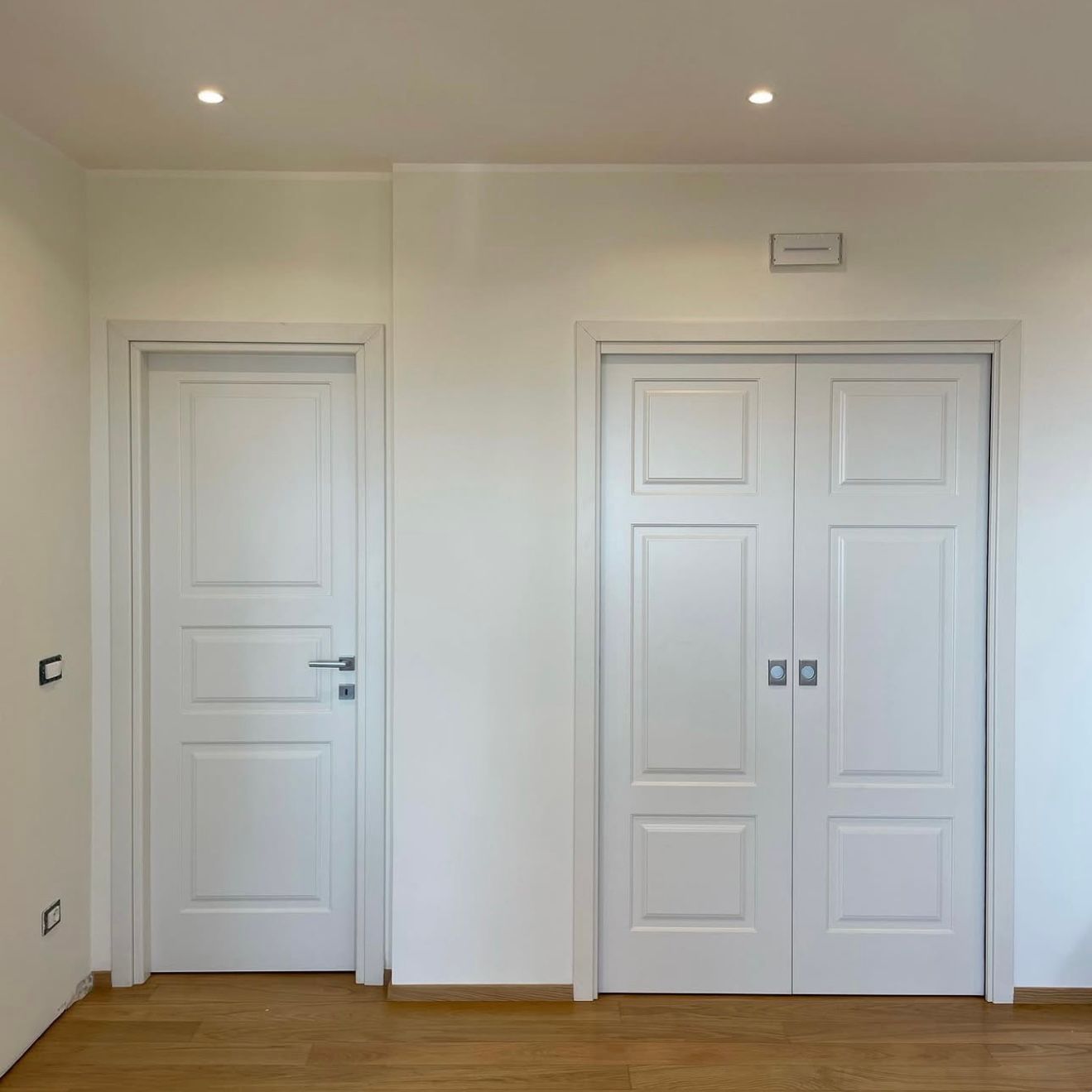 Una stanza con due porte bianche e un pavimento in legno.