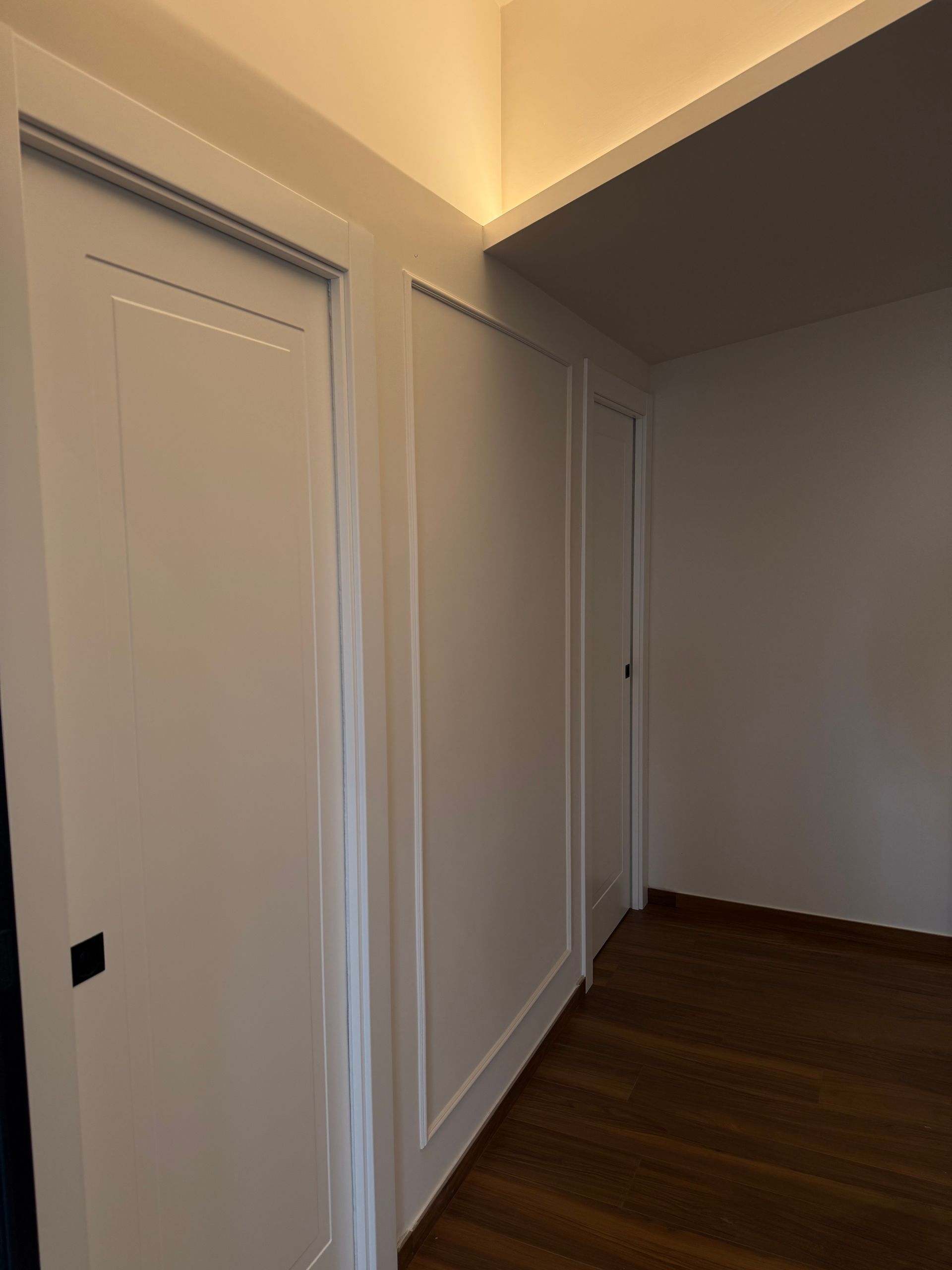 Un corridoio con due porte bianche e un pavimento in legno.