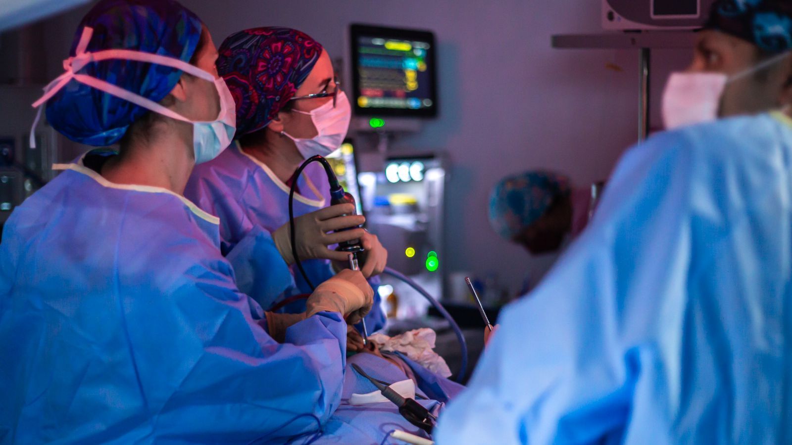 Medical team in blue scrubs operating with surgical instruments in a lit operating room.