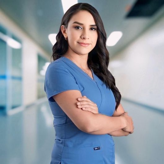 Una mujer con una blusa azul estรก parada en el pasillo de un hospital con los brazos cruzados.