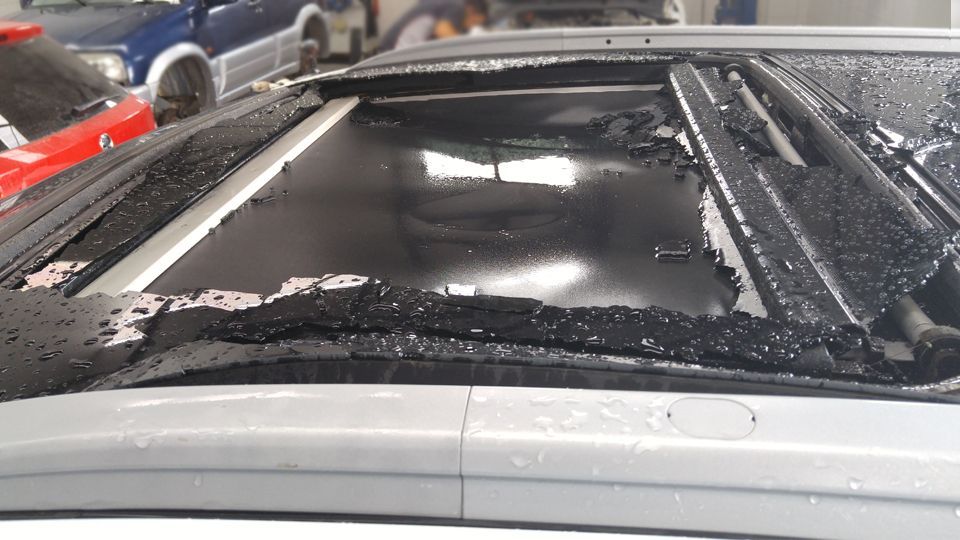 A car with a broken sunroof is parked in a garage.