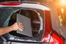 A person is holding a laptop out of a broken car window.