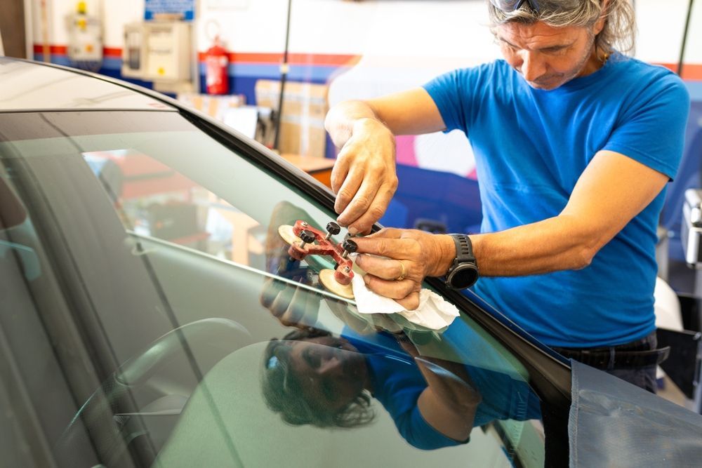A man is repairing a windshield on a car in a garage.