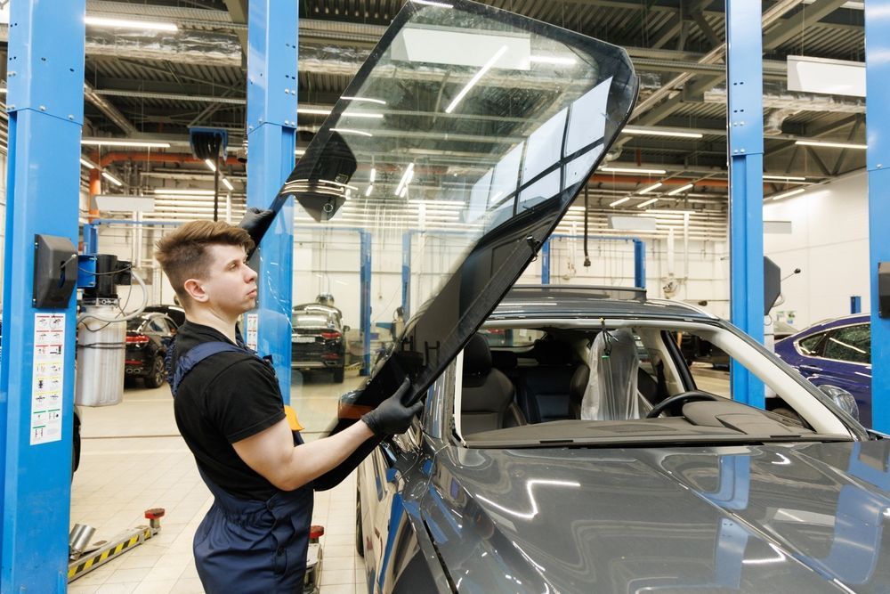 A man is installing a windshield on a car in a garage.