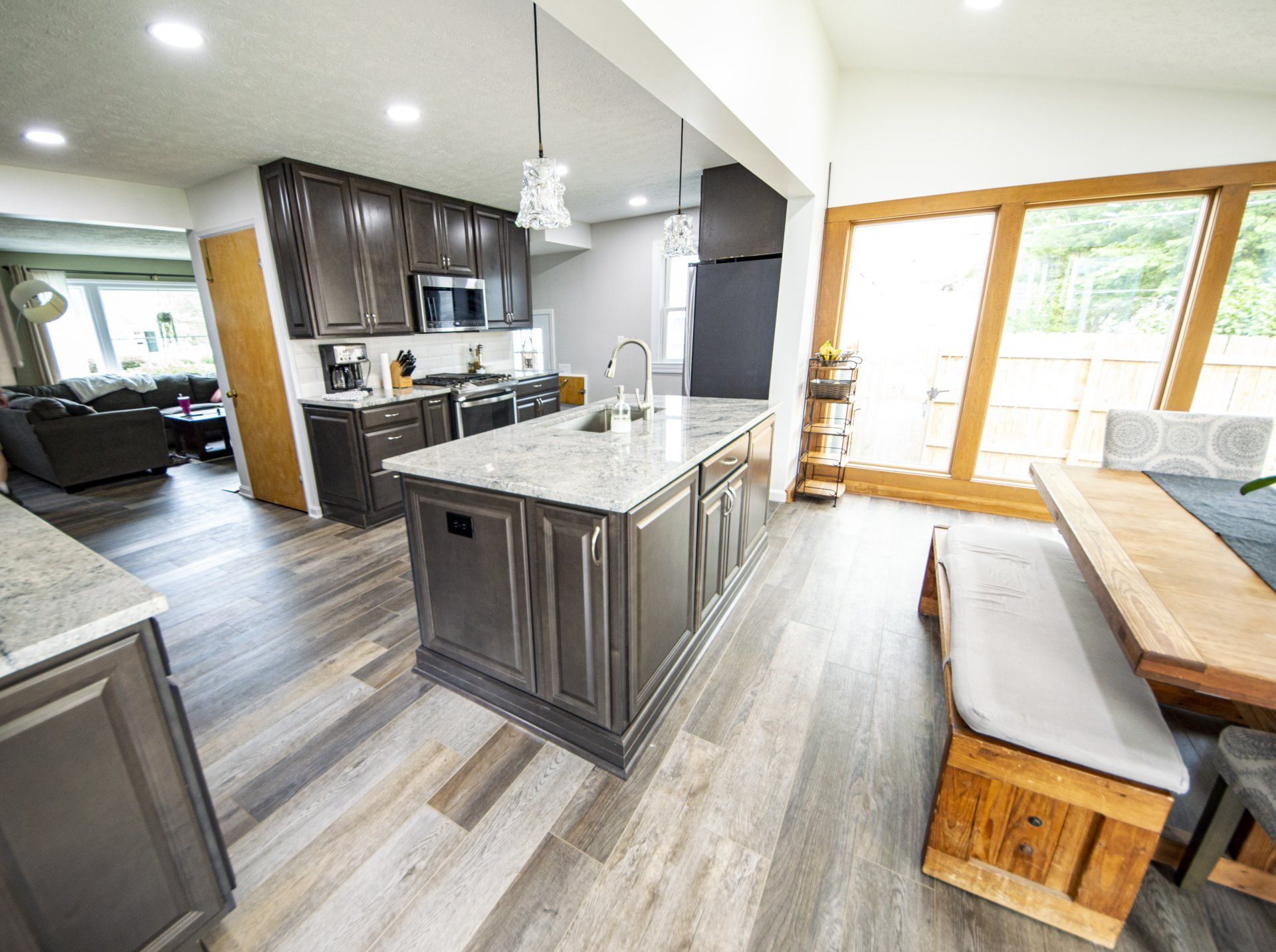 Kitchen with dark cabinets, large island, wood floor, and dining area with bench seating.