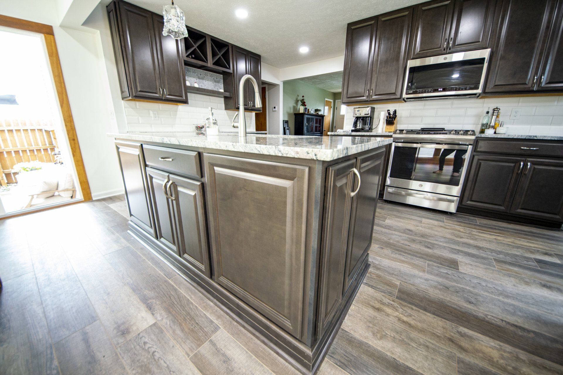 Modern kitchen with dark gray cabinets, island, stainless steel appliances, and light gray wood-look flooring.