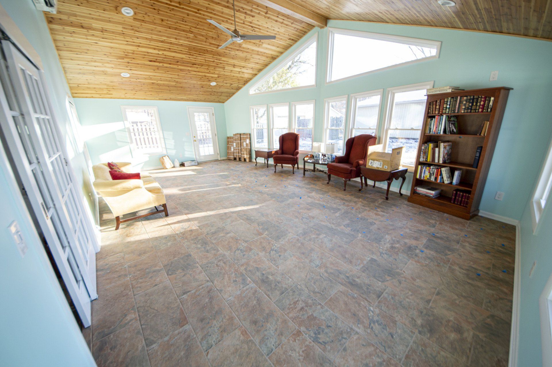 Spacious, light-filled room with vaulted wood ceiling, large windows, armchairs, and bookshelves.