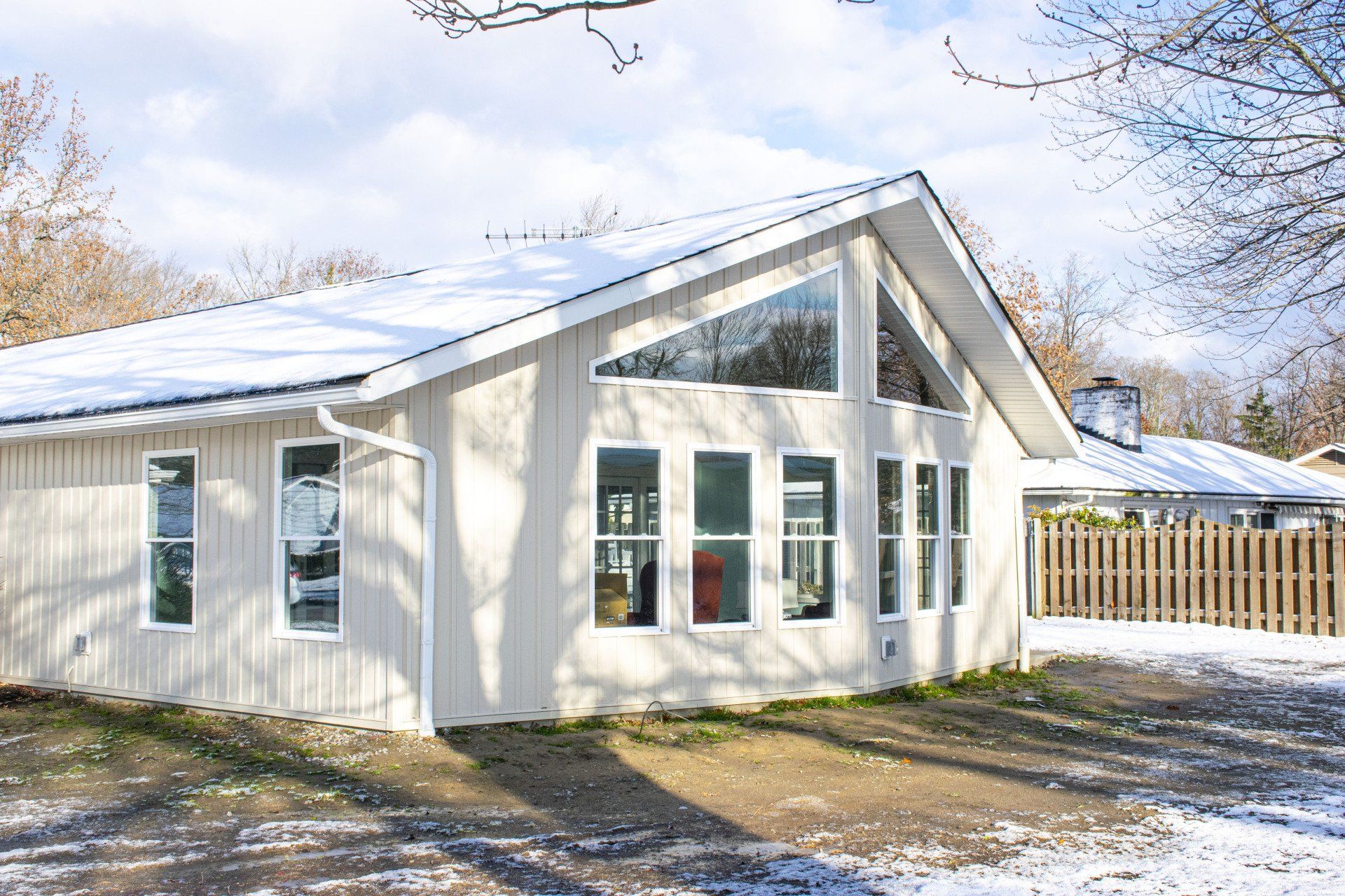 Snow-covered, light gray house with large windows under a blue winter sky.