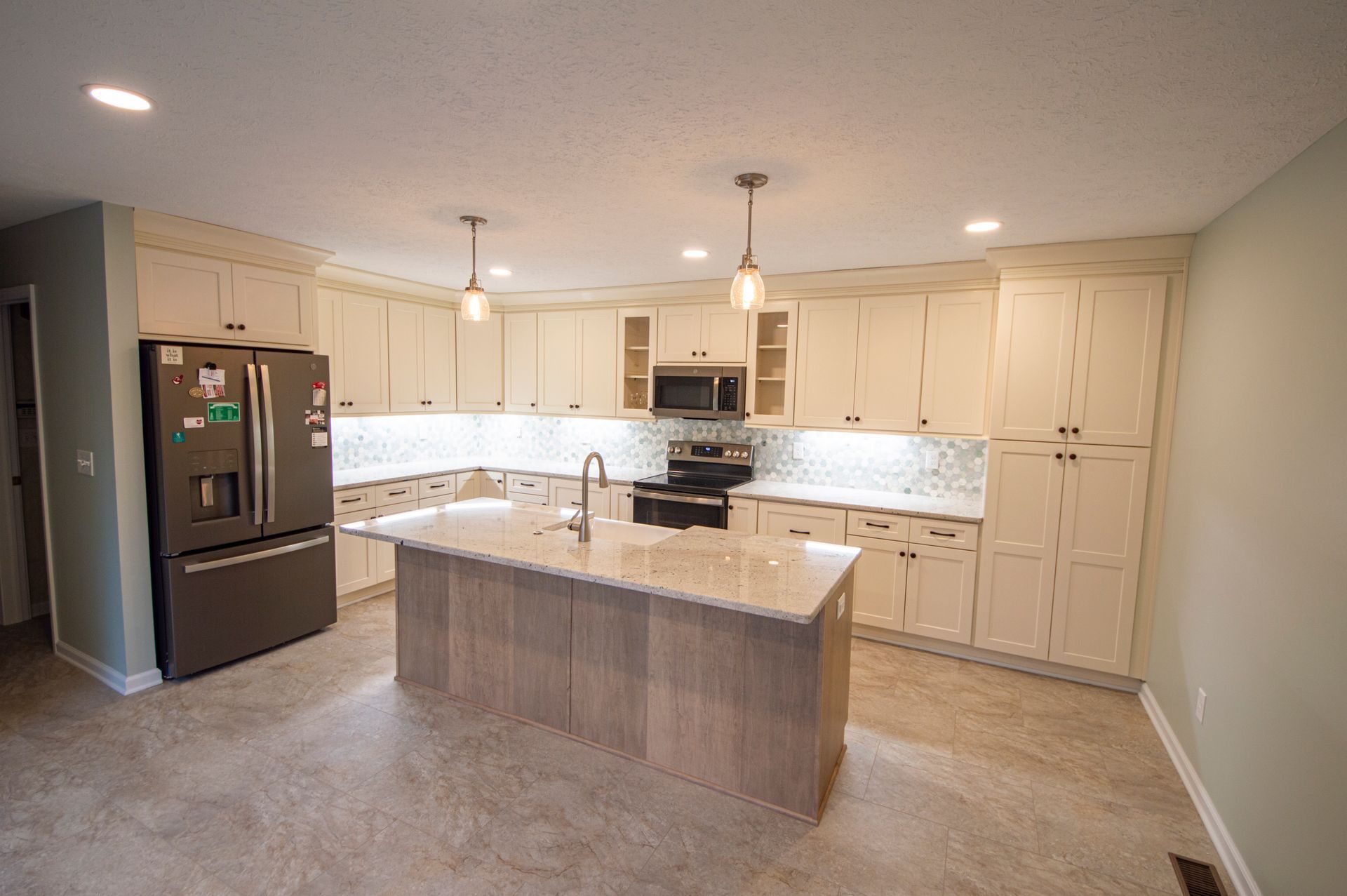 A modern kitchen with light cabinets, a central island, stainless steel appliances, and a light-colored countertop.